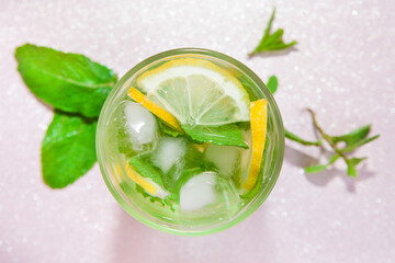 Lemonade drink or mojito cocktail with lemon, mint and ice on pink background from top view	