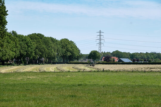 Dronten, the Netherlands June1,2021:Grassland with tractor mower and rake, grass ready to be ensiled.Dutch farmers race against the rain to hay,mow, rake and silage.All farmers are working on the land