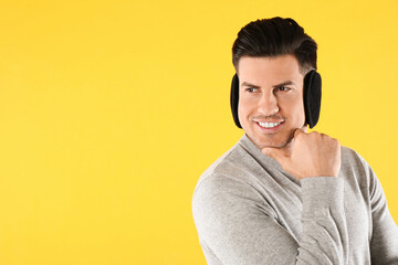 Man wearing stylish earmuffs on yellow background. Space for text