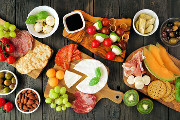 Italian theme charcuterie table scene against a dark wood background. Group of cheese, meat and fruit appetizers. Top view.