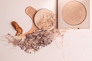 Crushed beige face finishing and liquid powder, smashed lipstick and cracked eyeshadow. Macro texture of make-up on beige background