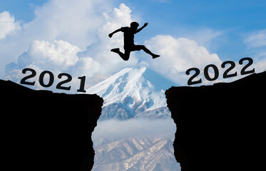 A young man jump between 2021 and 2022 years over the sky and cloud through on the gap of hill and...