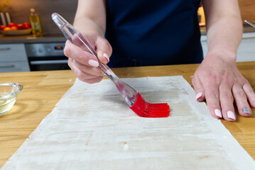 The process of making homemade pies with cottage cheese and dill. The cook greases the dough with a red brush with oil.