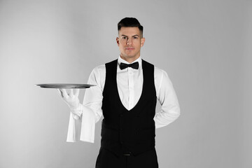 Handsome butler with tray on light grey background