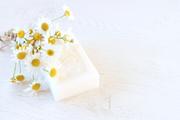 Hygiene product on a light background. Fresh chamomile flowers. Natural antioxidant, protection against bacteria - white soap with chamomile. Spa
