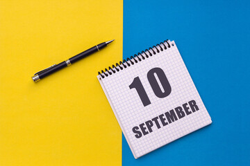 September 10th. Day 10 of month, calendar date. Notebook with a spiral and pen lies on a yellow-blue background