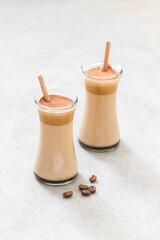 Milk cocktail with coffee cream in a glass with a bamboo straw on a light gray background	
