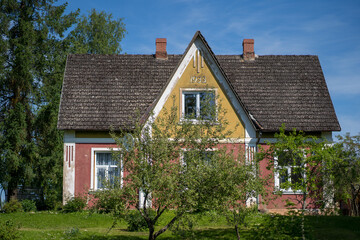 an old country house on a blue sky background, surrounded by various fruit trees and a green grass