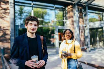 Young handsome caucasian curly man waiting for his girlfriend in the city street, outdoor. Love, relationship, dating: concept. French curly male student and african millennial female on background.