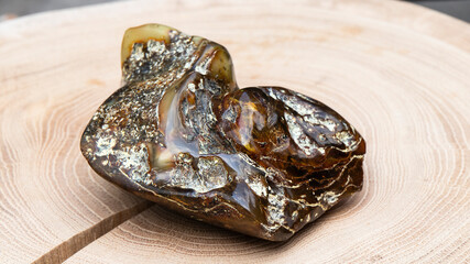 Big green and orange Baltic amber stone on a wooden surface. Material for jewelers, energy stone,...
