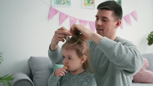 fatherhood, loving caring male parent does his daughter hair and ties her hair up with an elastic band, close-up