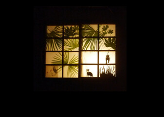 cutouts of plants and cats on windows illuminated by lights from the room