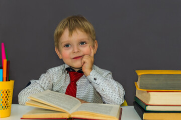 pensive preschool boy sitting at a Desk. Blond boy does his homework