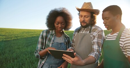 Group of multiracial farmers or technologists inspecting field process while using tablet computer for engineering. Cooperation and agriculture concept