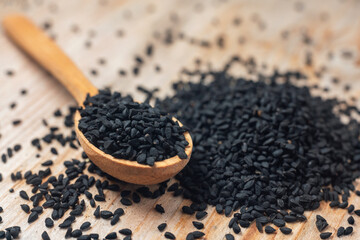 Black cumin seeds on wooden spoon on wooden background