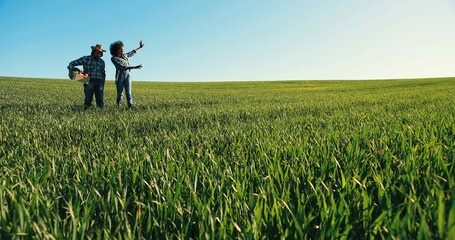 Two multiracial farmers walking on rural plantation field with lots of greenery. Proud farm owner working with his colleague at farmland during hot summer weather