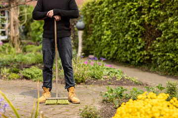 Man gardener wearing casual clothes leaning on a broomstick, having a break from cleaning the weeds...