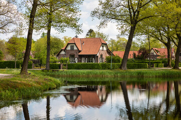 Fototapeta na wymiar Dutch authentic house near the river with reflections in the water, surrounded by trees and greenery on a sunny day during spring in Grientsveen, The Netherlands