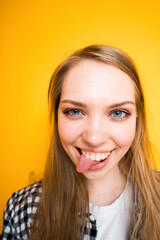 Portrait of a happy girl standing on a yellow background and sticking her tongue out to the side