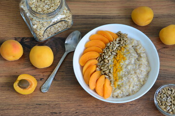 porridge with apricot, sunflower seeds and curcuma in white bowl with teaspoon and jar of oatmeal...