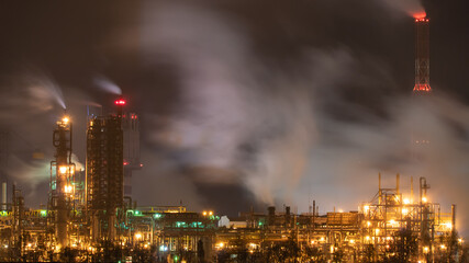 Fototapeta na wymiar View of a large factory or plant in the light of night lighting. A lot of smoke comes out of the factory's chimneys. Pollution of the environment. Toxic bad ecology