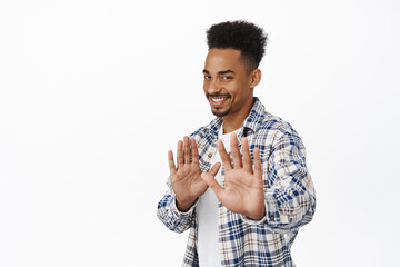 Smiling african american guy refusing politely, look awkward and raising hands in stop, no thank...