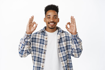 Fototapeta premium Image of smiling african american guy 20s showing okay, OK zero gesture and nod in approval, say yes, positive feedback, like and agree with you, praise choice, standing over white background