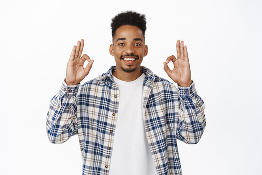 Image of smiling african american guy 20s showing okay, OK zero gesture and nod in approval, say yes, positive feedback, like and agree with you, praise choice, standing over white background