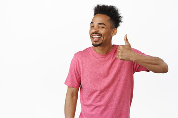 Nice choice. Smiling african american guy winking at you, showing thumb up in approval, praise...