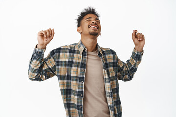 Naklejka premium Happy african american man dancing and enjoying party, raising hands up with carefree face expression, rejoicing, dance and have fun, standing against white background