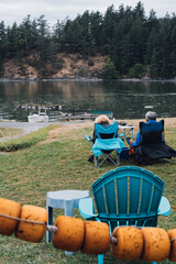 old man and woman coupe sitting in camp Adirondack chairs by water bay 
