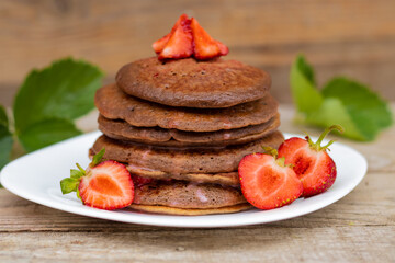 chocolate pancakes with strawberries, many, stack, on a white plate