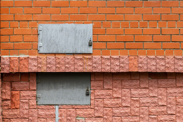 Two metal rectangular hatches in a red brick wall.