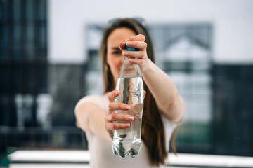 A beautiful young woman opens the lid of a plastic water bottle to drink it outside in the heat.