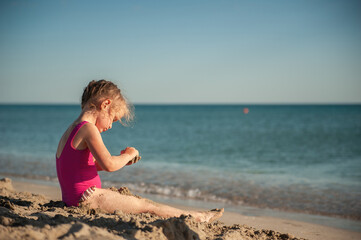 Fototapeta na wymiar Cute little girl playing in the sand on the sea beach