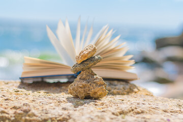 a pyramid of small stones and an open book on the background of the sea and rocks. summer vacation concept.