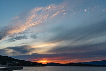 The sun just above the sea horizon creating a sunrise / sunset with a panorama of the mountains and rocky beaches