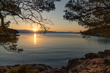 Fototapeta na wymiar The sun just above the sea horizon creating a sunrise / sunset with a panorama of the mountains and rocky beaches