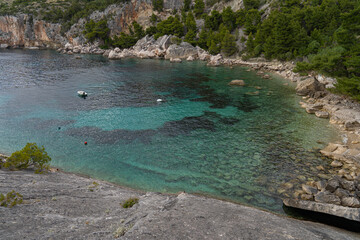 An atmospheric small rocky beach hidden between trees, rocks and turquoise sea water - obrazy, fototapety, plakaty