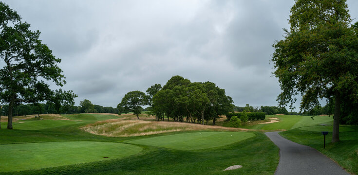 Panoramic landscape of tranquil golf course. Empty green field and trees with dramatic clouds.