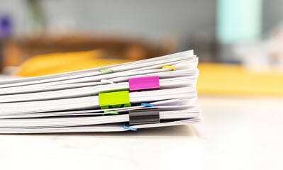 Pile of paperwork with colorful paper clips on office desk, blurred background. Administration of company's report information, organized job at workplace. Student’s research sheet stack on table.