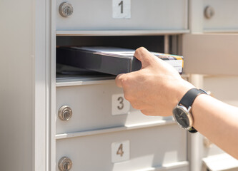 Mail man delivering small parcel in mailbox by house number, selective focus. Person’s hand holding package put in metal storage. People get packet from opened cabinet door. Sender, receiver concept.