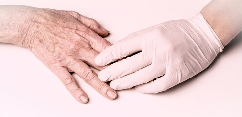 Obraz premium A doctor's hand in a white glove holds the hands of an elderly woman, a patient. Handshake, caring, trust and support. Medicine and healthcare.