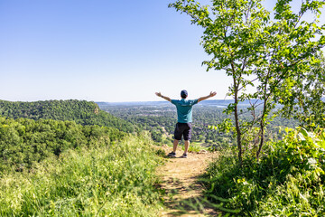 Man open arms after hiking to a peak of mountains with beautiful scenic of greenery forest and clear blue sky. Outdoor adventure activity with nature travel lifestyle. Leisure, relaxation and freedom