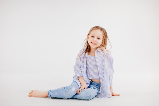 little girl with long hair in jeans and shirt posing against a white background.