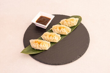 Chinese dumplings, dim sum, steamed with soy sauce on the side on a round black slate plate and banana leaf