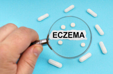 A man looks through a magnifying glass at pills and a leaf with the inscription - ECZEMA