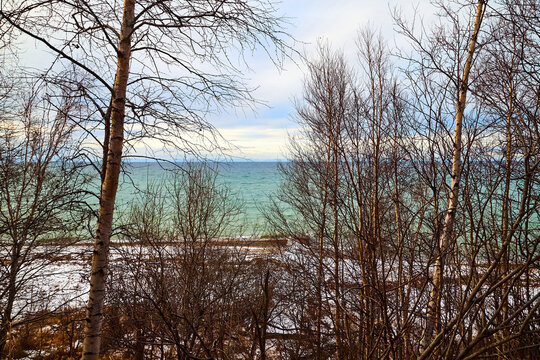 Nature landscape with dramatic sky and clouds, lake with ice, shore with snow and dark trees without leaves in cold winter or autumn day or evening