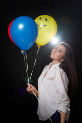 Beautiful girl with long hair and with colored balloons posing in studio on a black background