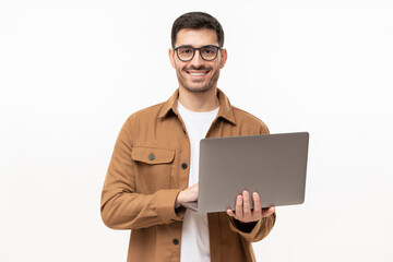 Studio portrait of young man standing holding laptop and looking at camera with happy smile,...